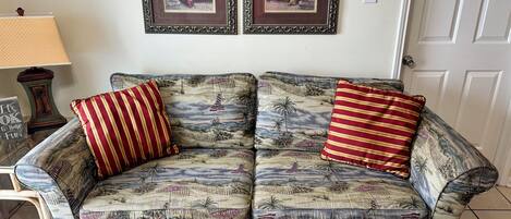 A patterned sofa with striped pillows, a lamp, and two framed artworks on the wall.