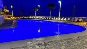 An outdoor swimming pool at night with a paved deck, lounge chairs, and palm trees. - Reduced rates!!  A+ Spectacular Beach Front Condo! 2BR 2BA!  Sleeps up to 6. (Orange Beach)