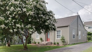 Una casa a un piano con una porta rossa, un piccolo portico e un albero con fiori bianchi.