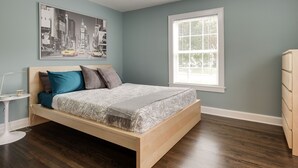 Una camera da letto con un letto in legno, un quadro che raffigura un panorama urbano, una finestra con persiane e un comodino con una lampada.