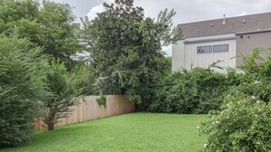 Un giardino recintato da una staccionata, con prato e una casa con garage.