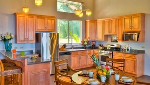 A modern kitchen with wooden cabinets, stainless steel appliances, and a dining area with a round table and chairs. - Villa Sirenetta-Minutes from the beach! (Tortola)