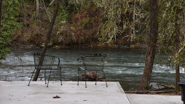 A concrete deck with two metal chairs facing a river.
