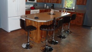 A kitchen with wooden cabinets, a white refrigerator, a microwave, a stove, and a large island with bar stools.