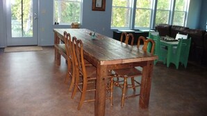 A dining area with a wooden table and chairs, large windows, a green chair, and a brown couch.