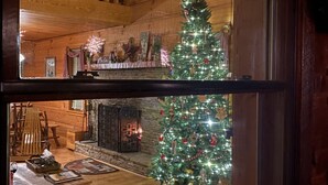 Acogedor interior de cabaña con paredes de madera, chimenea y un árbol de Navidad.