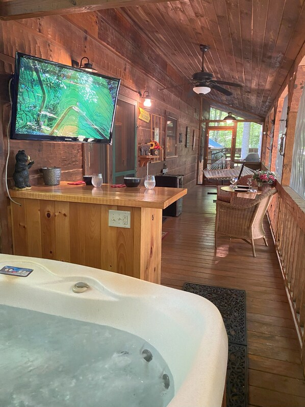 L'intérieur d'un chalet en bois comprend un bar en bois, un grand écran de télévision, un jacuzzi, des meubles en osier et une vue sur l'extérieur.