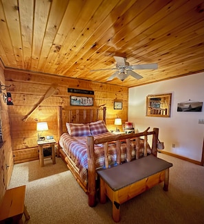A cozy log cabin bedroom with a bed, a bench, a ceiling fan, and a wall-mounted sign. - Luxury Log Cabin on Edge of National Park with Over-The-Top Amenities & Reviews (Cosby)