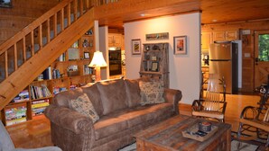 A cozy living room with a wooden staircase, a sofa, a coffee table, and a bookshelf filled with books.