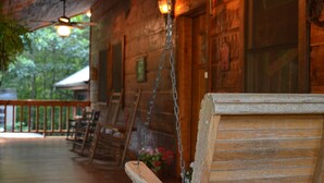 A wooden porch with a swing, hanging lights, and a view of the surrounding trees.