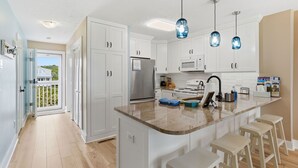 A kitchen with white cabinets, a stainless steel refrigerator, a microwave, and a large island with bar stools.