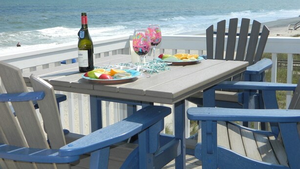 A wooden deck with a table set for two, featuring a bottle of wine, glasses, and a plate of fruit.