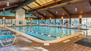 An indoor swimming pool with clear lane dividers, a stone pillar, and a view of the outdoors through large windows.