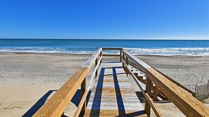 A wooden boardwalk leading to a beach with clear blue water.