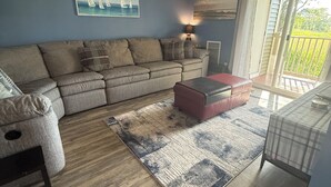 Un salon doté d’un ventilateur de plafond, d’un canapé, d’une table basse, d’un tapis et offrant une vue à travers une porte vitrée.