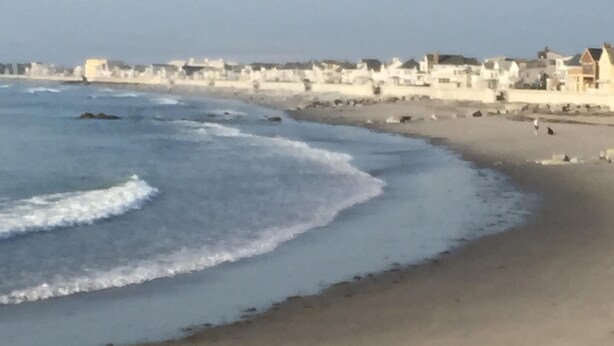 Une plage avec des vagues, une étendue de sable et des bâtiments en arrière-plan.