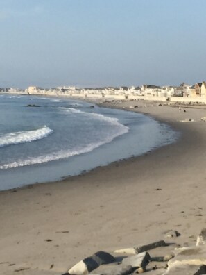 Una playa con olas, una orilla arenosa y edificios al fondo.