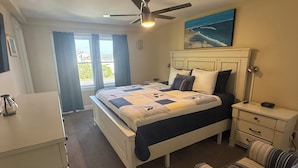Une chambre à coucher comprenant un lit, une table de chevet, une chaise, un ventilateur de plafond et une fenêtre avec des rideaux.