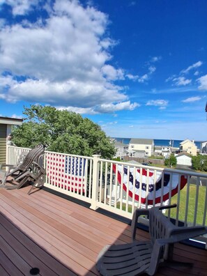 A wooden deck with a railing, two chairs, and an American flag. - Now renting summer of 2027 (Hampton)