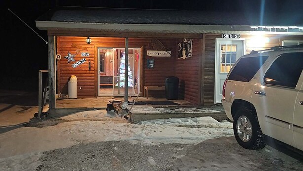 A cabin with a wooden exterior, a porch, a mailbox, and a parked SUV.