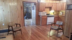 A wooden interior with a kitchen area, two chairs, and a small table.