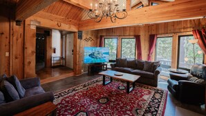A wooden interior with a chandelier, sofas, a TV, and large windows. - Tahoe Lodge Style Ambiance, Dog Friendly with Hottub, Sauna & Fenced Yard. By Tahoe Time VR (Tahoe City)