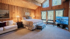 A bedroom with a large bed, a sofa, a TV, and a window with a view of trees. - Tahoe Lodge Style Ambiance, Dog Friendly with Hottub, Sauna & Fenced Yard. By Tahoe Time VR (Tahoe City)