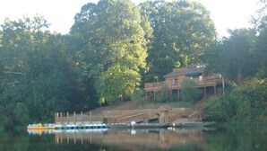 Un chalet au bord du lac, doté d’une terrasse en bois, d’un quai pour bateaux et d’un bâtiment surmonté d’un toit végétalisé.