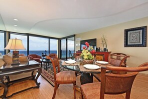 A dining area with a table set for four, surrounded by wicker chairs, a decorative vase, and a view of the ocean through large windows.