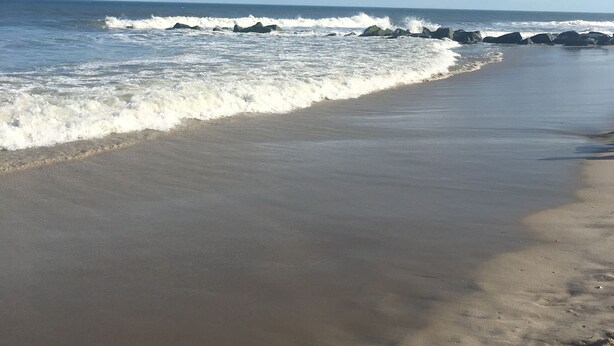 Uma praia com ondas quebrando na costa e um céu azul claro.