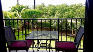 A balcony with two wicker chairs and a small table, overlooking a garden with various trees and shrubs. - Your paradise - entire > 800 square feet apartment with affordable rate  (Kihei)