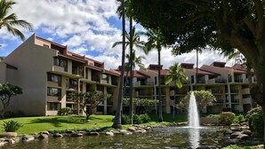A hotel with multiple balconies, a pond with a fountain, and lush greenery. - Your paradise - entire > 800 square feet apartment with affordable rate  (Kihei)