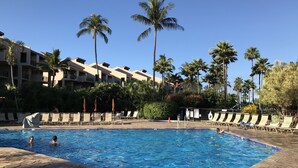 A swimming pool with lounge chairs and palm trees, surrounded by a building with balconies. - Your paradise - entire > 800 square feet apartment with affordable rate  (Kihei)