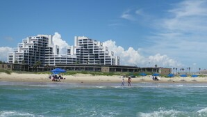 Een strandhotel met meerdere gebouwen, een zandstrand en golven.