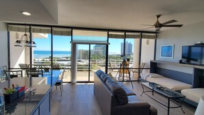 Een moderne woonkamer met een grote glazen deur die leidt naar een balkon, een bank, een televisie en een eethoek met een tafel en stoelen.