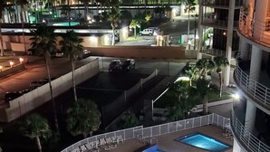 Zwembad op een dak met een gebogen ontwerp, omringd door palmbomen en ligbedden, met een stadsbeeld op de achtergrond bij nacht.