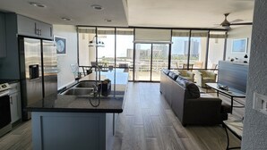 Een moderne keuken met een centraal eiland, een eethoek met een glazen tafel en een zithoek met een bank en stoelen.
