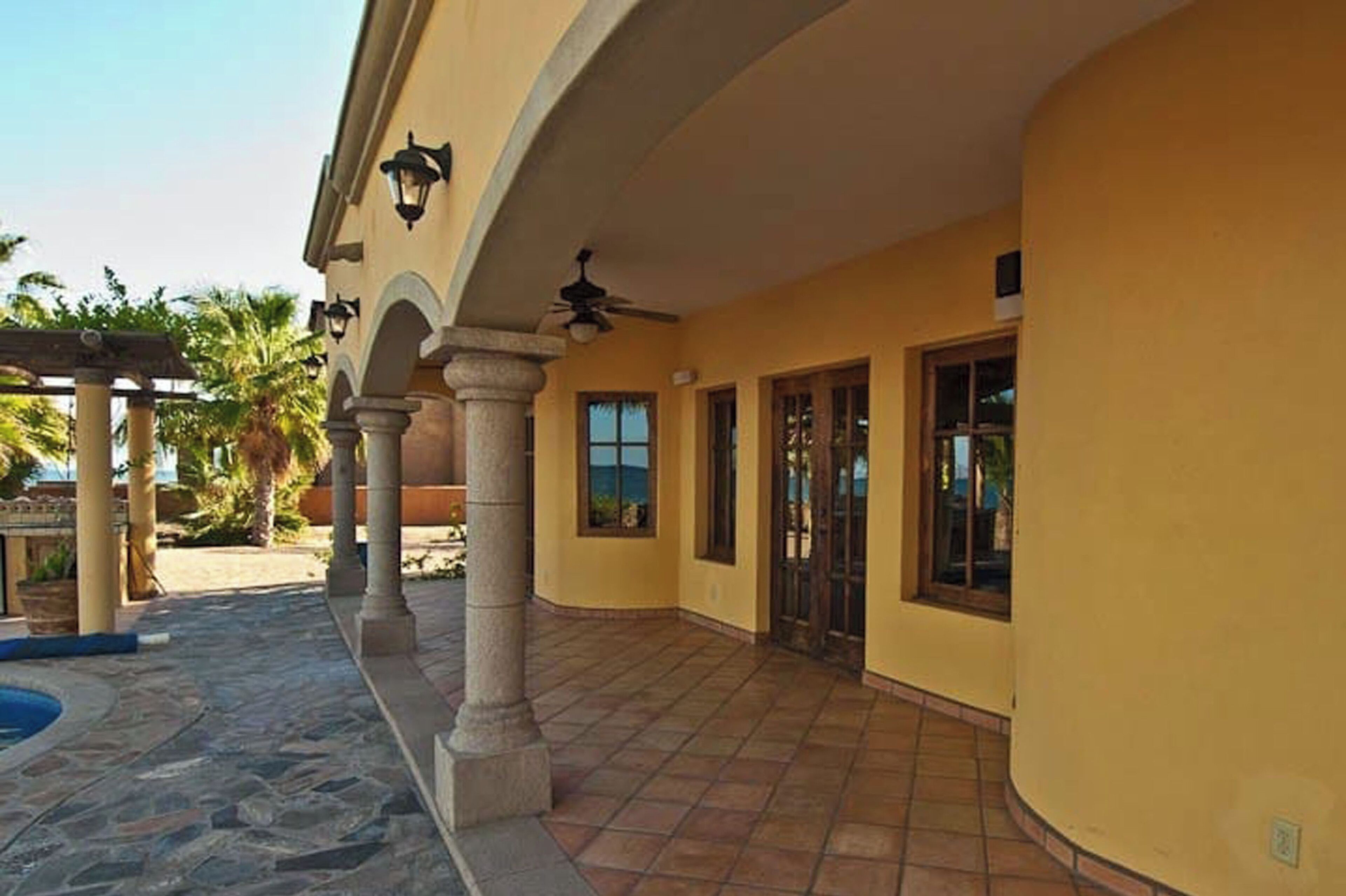 A building with a covered patio area, stone flooring, and a pool.