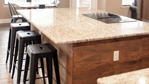 Una cucina moderna con una grande isola, sgabelli da bar, una ventola a soffitto e vista all'esterno tramite ampie finestre.