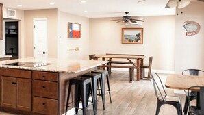 Una cucina moderna con isola centrale, sgabelli da bar, tavolo da pranzo e ventilatore a soffitto.