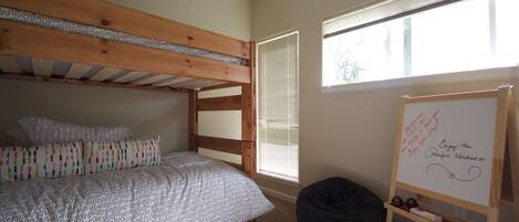 A bunk bed with patterned bedding, a whiteboard with writing, and a bean bag chair in a room with a large window.