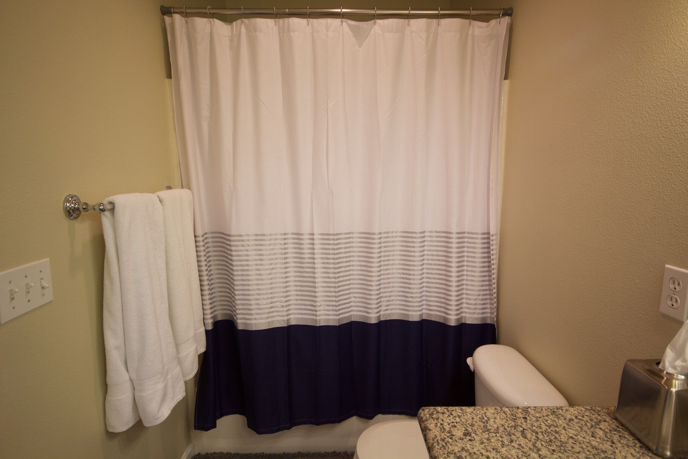 A bathroom with a white and navy shower curtain, a white toilet, and a granite countertop.