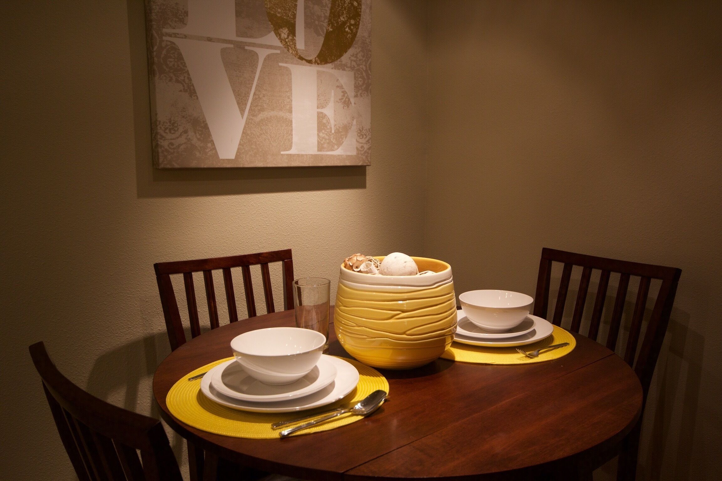 A dining table with white bowls, a yellow bowl with ice cream, and a spoon.