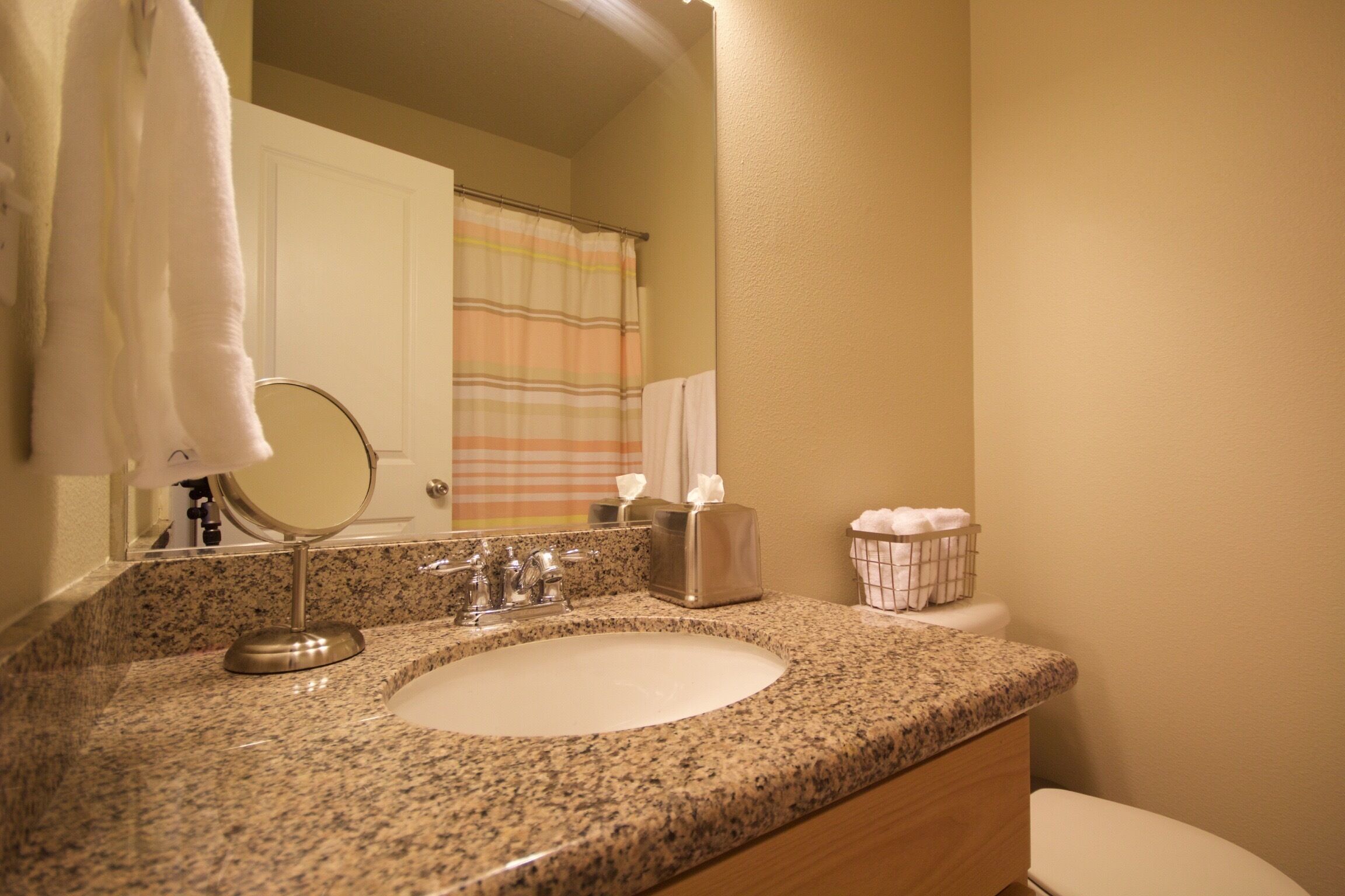 A bathroom with a granite countertop sink, a mirror, a towel rack, a toilet, and a shower curtain.