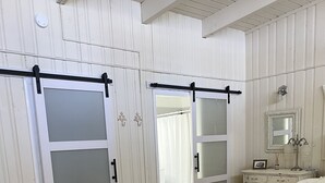Makuuhuoneessa on puulattia, valkoiset seinät, valkoisilla lakanoiden päällisillä varustettu sänky, lipasto, peili ja liukuovi, jossa on himmeät lasipaneelit.