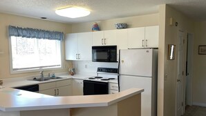 Una cocina con armarios blancos, un microondas negro, un refrigerador blanco y una ventana con vistas al exterior.