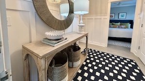 A hallway with a wooden console table, a white bowl, and a mirror. There is a bed with pillows and a ceiling fan in the background. - Gulf-front,Pool,Balcony, VIEWS, 30A, Private Beach, Grill (Santa Rosa Beach)