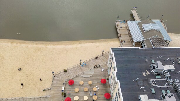 A high vantage view of a waterfront hotel with a wooden deck, outdoor seating, and a view of the adjacent beach. - Downtown Dewey Beach Ocean/Bay Views 2BR Pools Fire Pit (Rehoboth Beach)