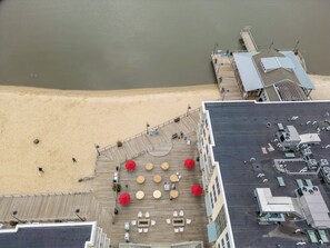 Vista panorámica desde lo alto de un hotel frente al mar, con muelle de madera, mobiliario exterior y vistas a la playa contigua.