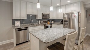A modern kitchen with white cabinets, stainless steel appliances, granite countertops, and pendant lighting. - Downtown Dewey Beach Ocean/Bay Views 2BR Pools Fire Pit (Rehoboth Beach)